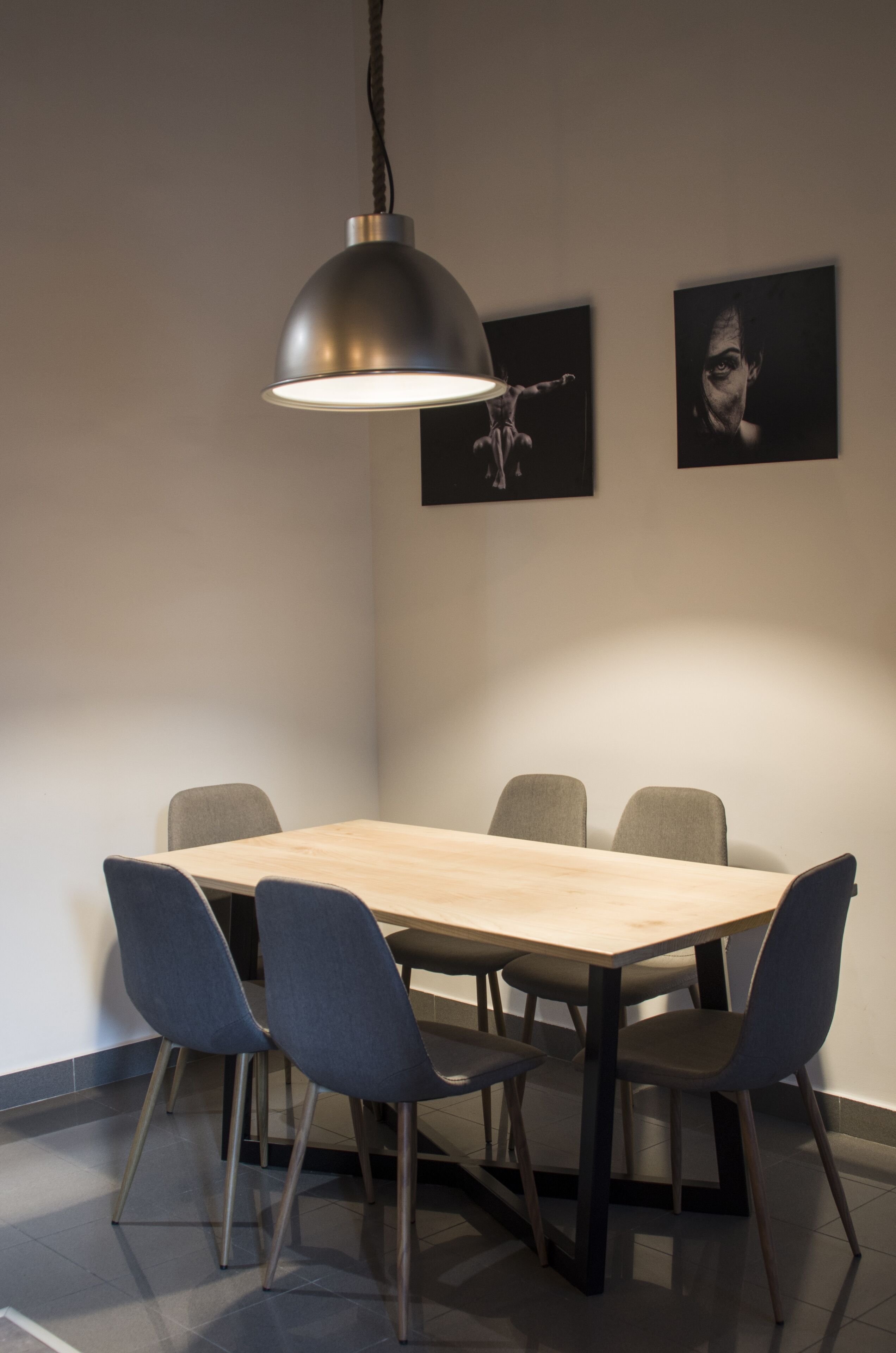 A modern dining area with a wooden table and six chairs, a pendant light, and two framed artworks on the wall.