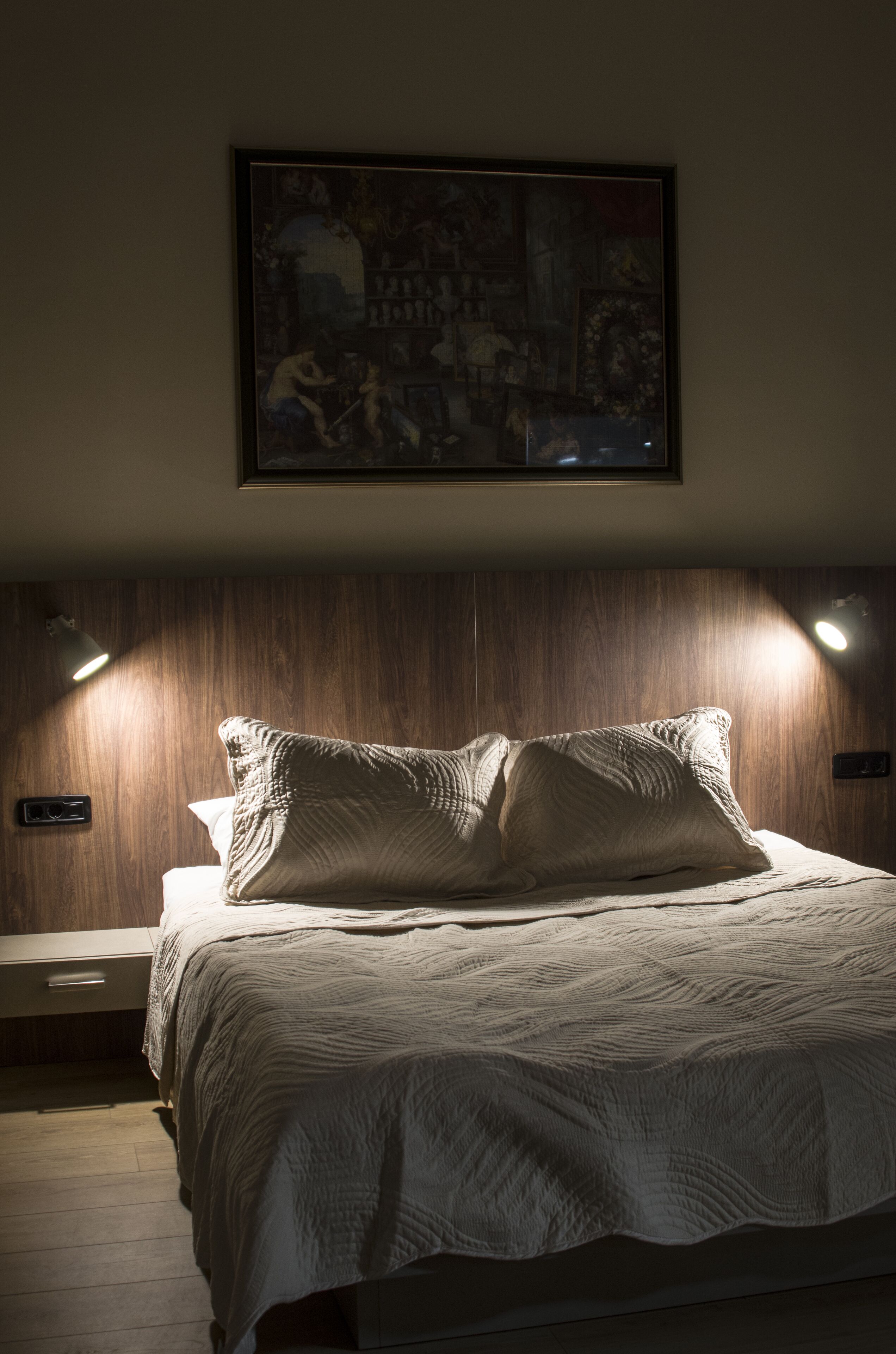 A bedroom with a bed, a wooden headboard, and a painting above the bed.