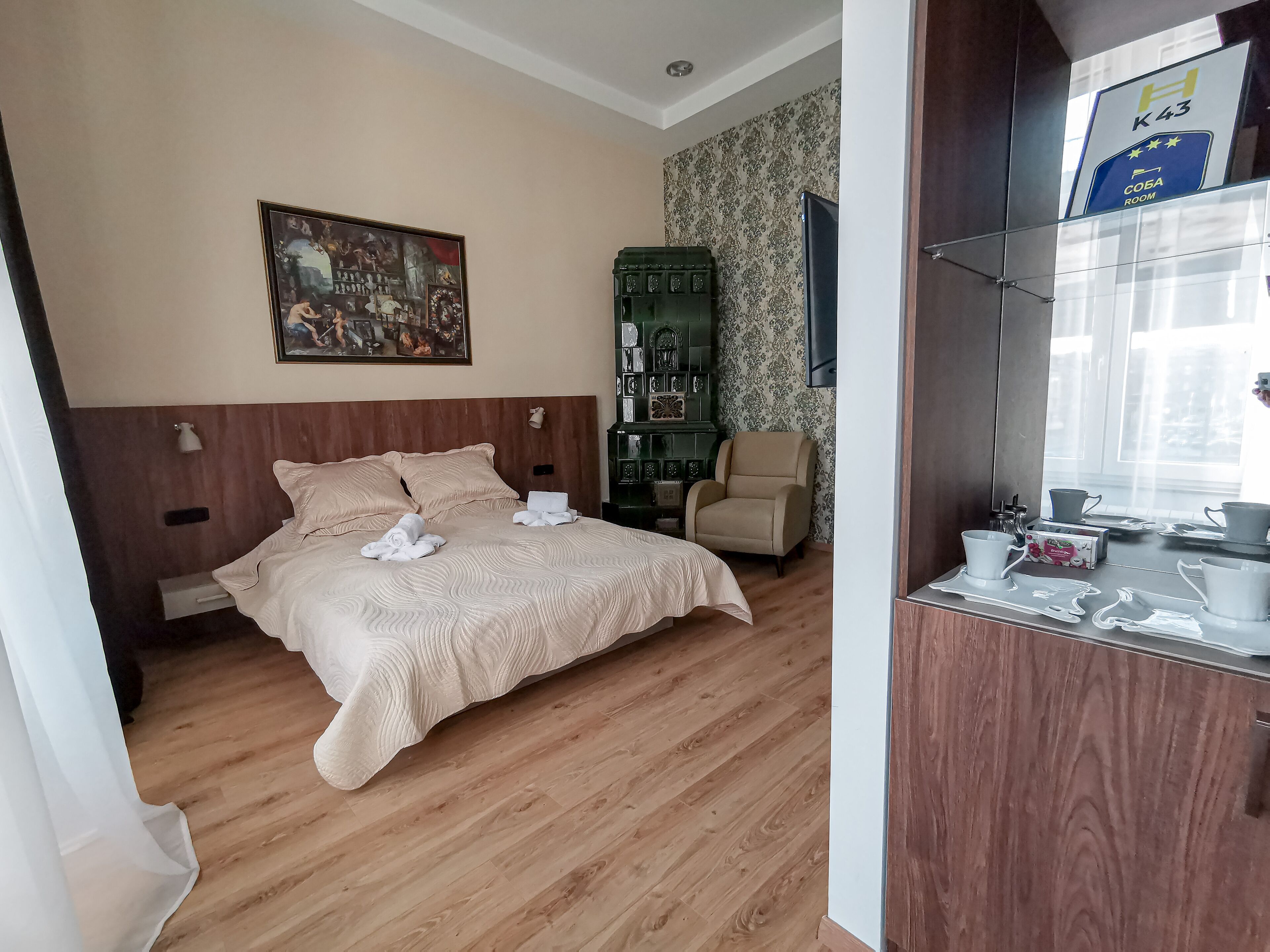 A hotel room with a bed, a chair, a TV, and a minibar.