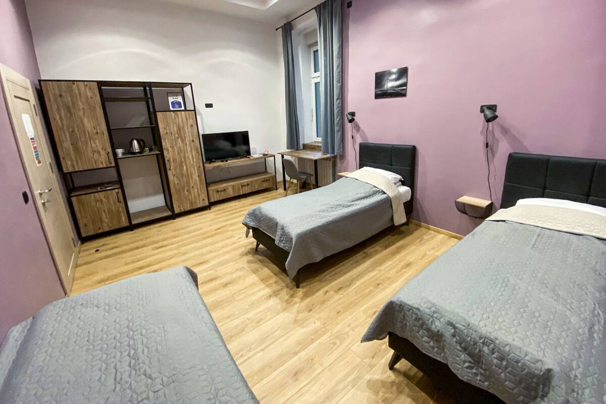 A hotel room with two beds, a desk with a chair, a wardrobe, and a television.