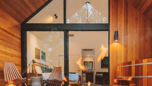 A modern wooden cabin with a large glass window, a fireplace, and outdoor seating. - Kuono at Volcano   . (Volcano)