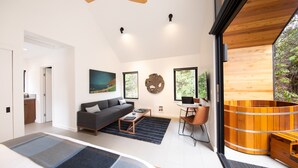 A modern living room with a sofa, coffee table, and a wooden hot tub. There are large windows and artwork on the walls. - Kuono at Volcano   . (Volcano)