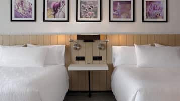 A hotel room with two beds, a small table, and a wall-mounted lamp.