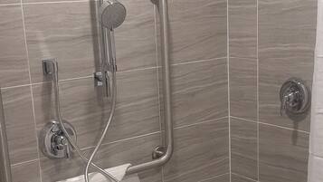 A shower area with a handheld showerhead, a wall-mounted showerhead, and a towel rack.