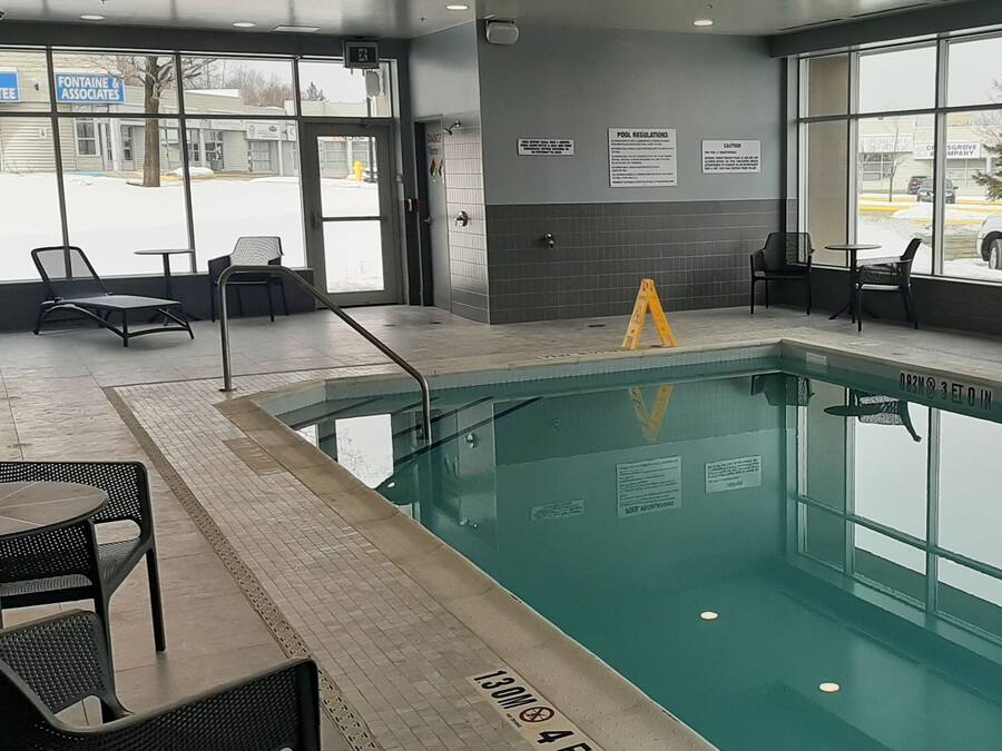 An indoor swimming pool with clear pool regulations signs, a lifeguard chair, and lounge chairs around the pool area.
