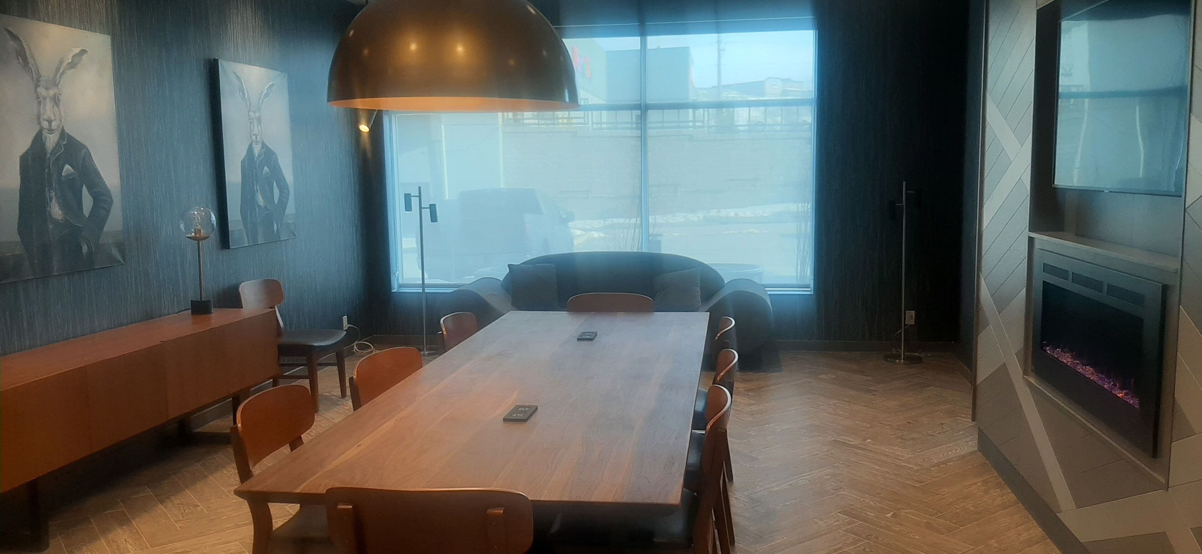 A modern meeting room with a wooden table, chairs, a large pendant lamp, and artwork on the walls.