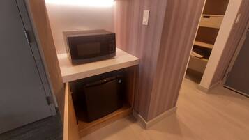 A compact kitchen area with a microwave on a shelf, a small refrigerator below, and a wooden cabinet.
