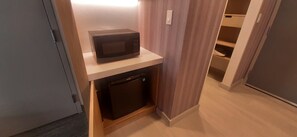 A compact kitchen area with a microwave on a shelf, a small refrigerator below, and a wooden cabinet. - Hilton Garden Inn Sudbury (Sudbury)