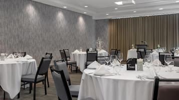 A conference room with round tables, each set with white tablecloths, chairs, and glassware.