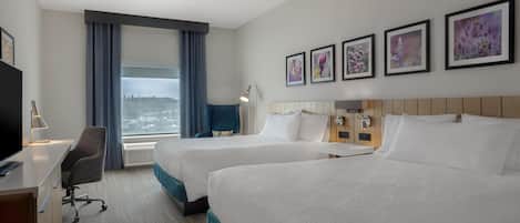 Habitación de hotel con dos camas, un escritorio con silla, televisión y un ventanal con cortinas.