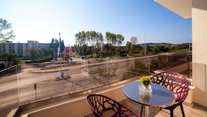 A balcony with a round table and chairs, overlooking a road with a roundabout and trees.