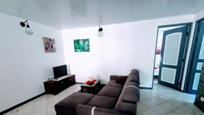 Una sala de estar con un sofá modular, un televisor de pantalla plana sobre un mueble bajo, una mesita con un objeto decorativo y un cuadro en la pared.
