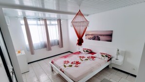 Un dormitorio moderno con cama, cortinas, un dosel rojo colgante, una mesita de noche, una lámpara y un cuadro en la pared.