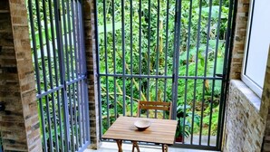 Un pequeño balcón con una mesa y sillas de madera, rodeado por una reja de metal y muros de piedra.
