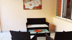 Un pequeño espacio al aire libre con un sofá negro, dos sillas de mimbre y una mesa con un plato decorativo.