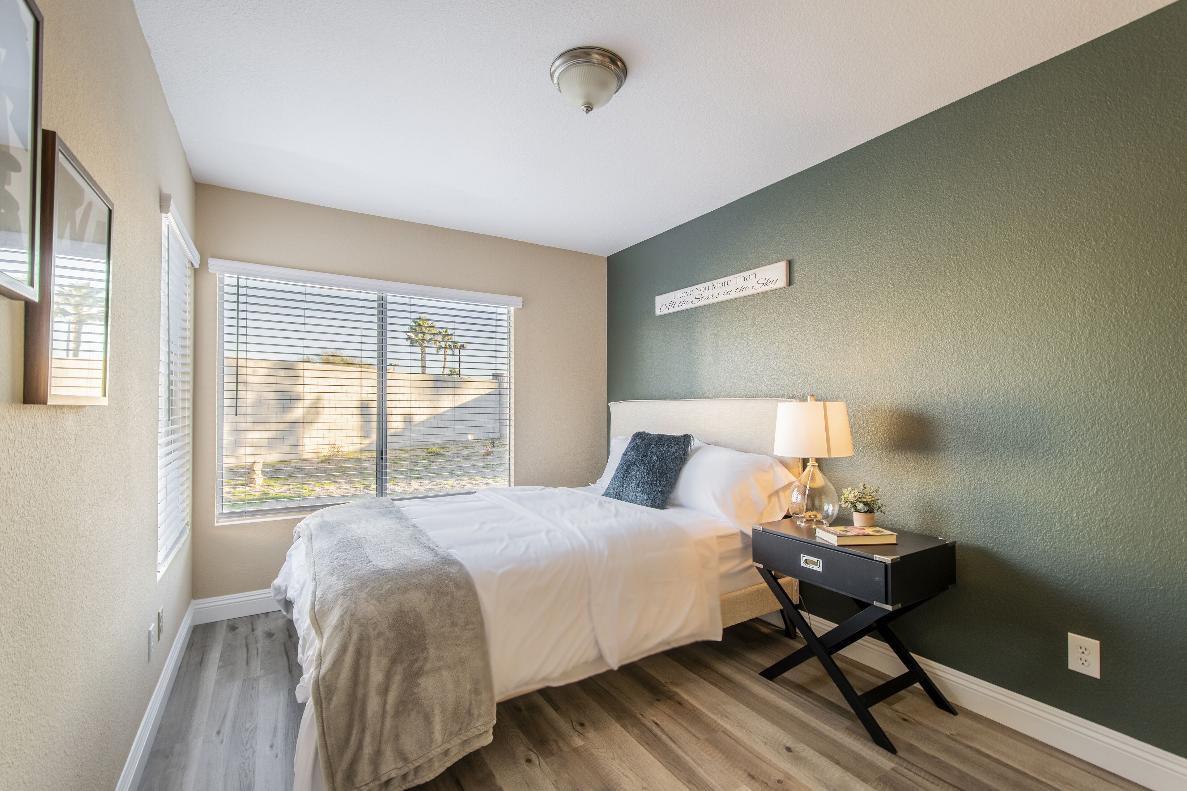 A bedroom with a bed, bedside table, lamp, and a wall-mounted sign.