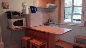 Eine kompakte Küche mit Mikrowelle, Toaster und kleinem Kühlschrank. Holzstühle und ein Fenster mit Blick nach draußen.