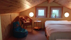 Ein gemütliches Schlafzimmer im Dachgeschoss mit einem Bett, einem Schaukelstuhl, einem kleinen Tisch und zwei mit Vorhängen versehenen Fenstern.