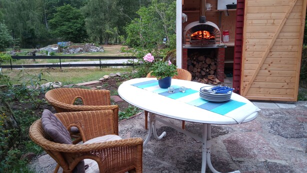 Eine Terrassengaststätte mit Korbstühlen, einem Tisch mit blauen Tischsets und einem Holzofen für Pizza.