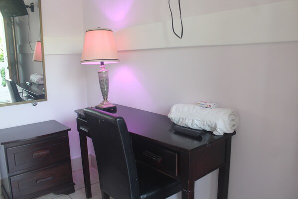 A room with a desk, a chair, a lamp, a mirror, and a towel on the desk.
