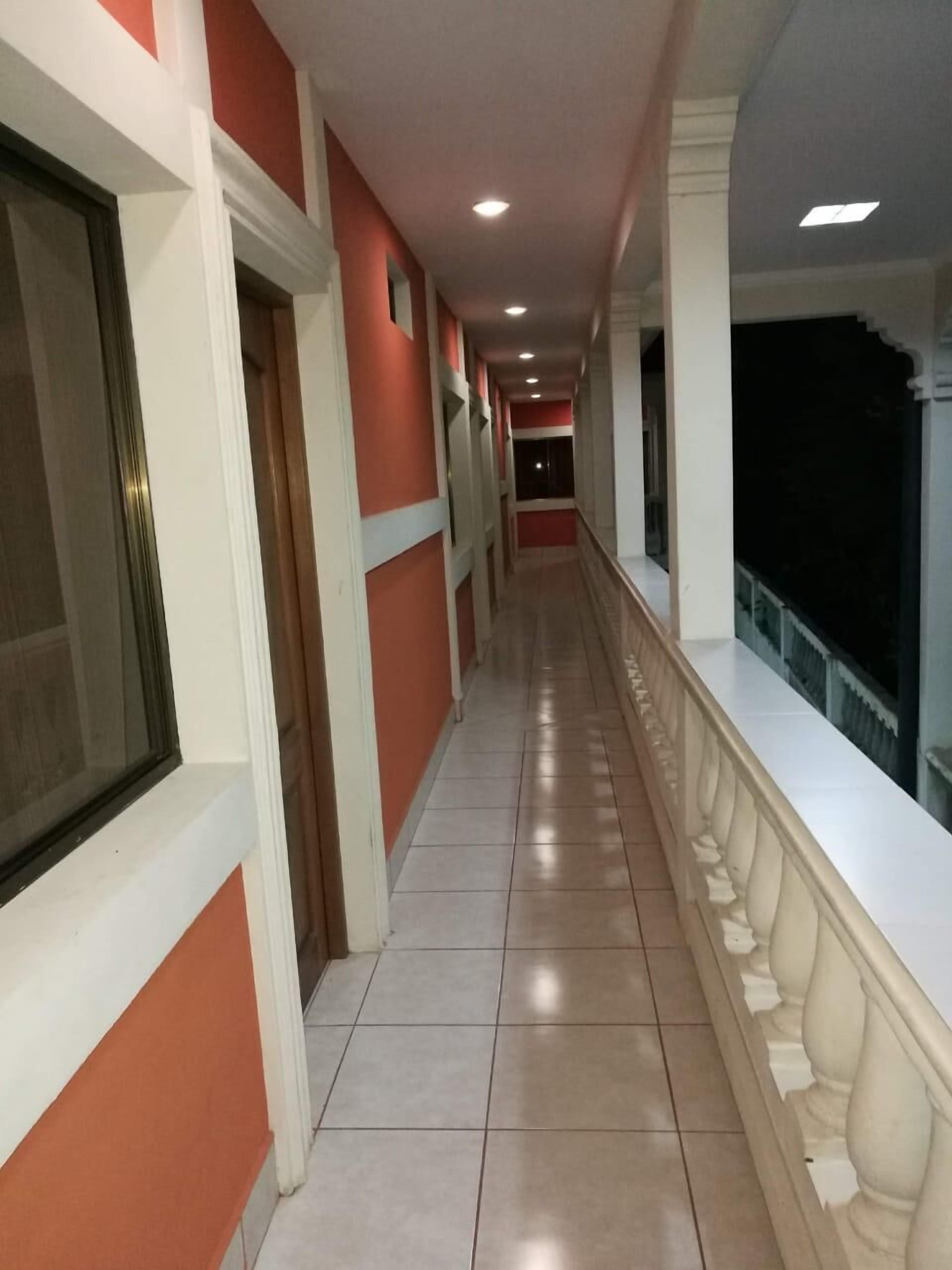 A corridor with tiled flooring, white and red walls, and a balcony with a balustrade.