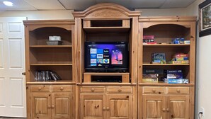 Centro de entretenimento de madeira com televisão de tela plana, prateleiras com livros e jogos, e uma porta à esquerda.