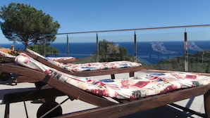 A balcony with two sun loungers, one with a Union Jack pattern, overlooking a coastal view with the sea and distant land. - Apartment OCEAN AND FOREST VIEWS WITH PRIVATE POOL (2 rooms) (Blanes)