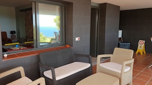 A balcony with wicker furniture, a window with a view of the sea, and a caution sign. - Apartment OCEAN AND FOREST VIEWS WITH PRIVATE POOL (2 rooms) (Blanes)
