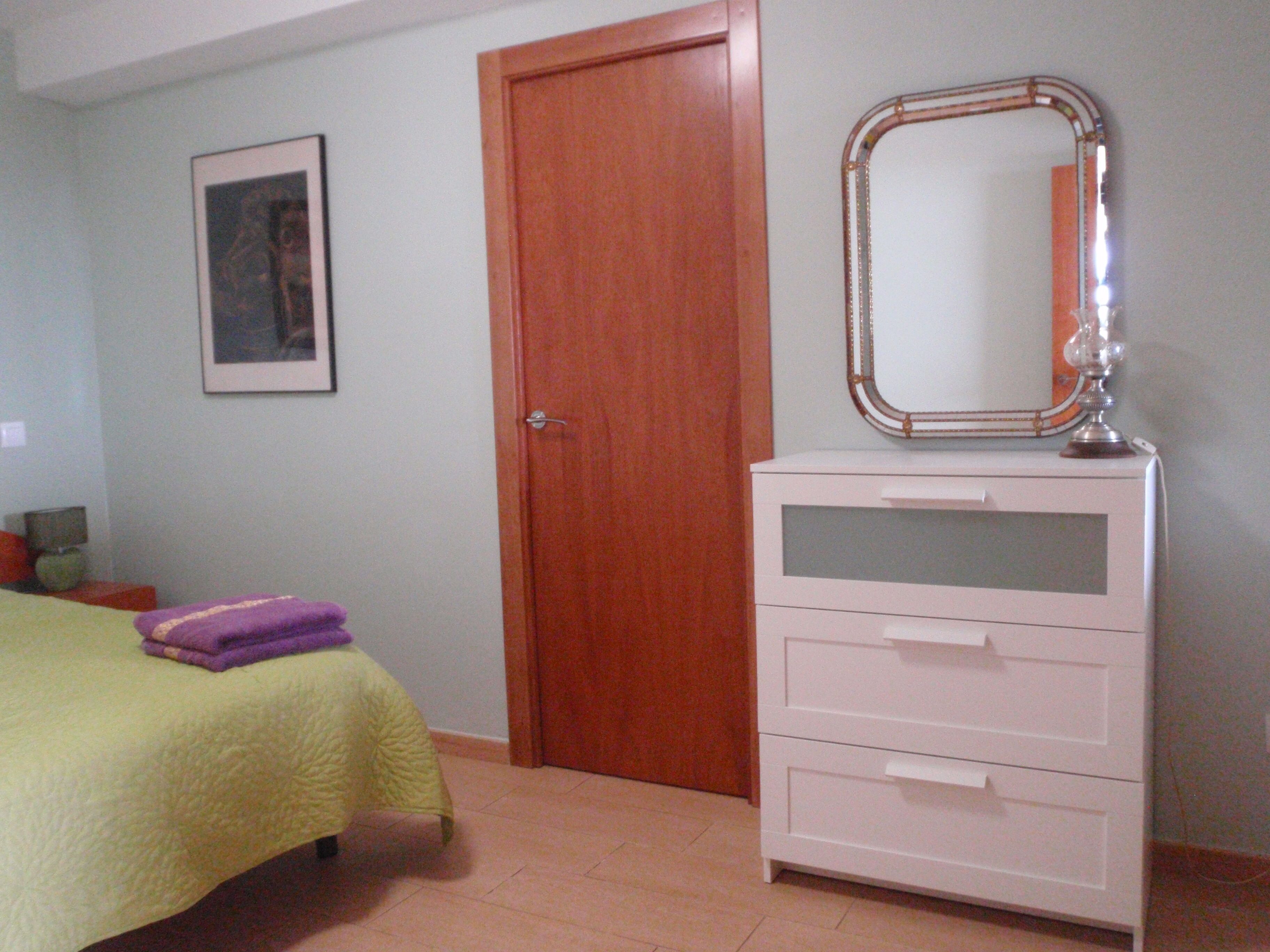 A bedroom with a bed, a dresser, a mirror, and a door.