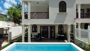 A two-story building with a pool, outdoor seating, and a white fence.