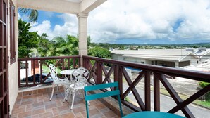 A balcony with a white table and chairs, a view of a residential area, and a clear sky.