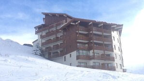 Een hotel met meerdere verdiepingen, houten balkons en een skipiste op de achtergrond.