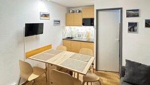 Een knus woongedeelte met een eethoek, een kitchenette en een grijze bank.