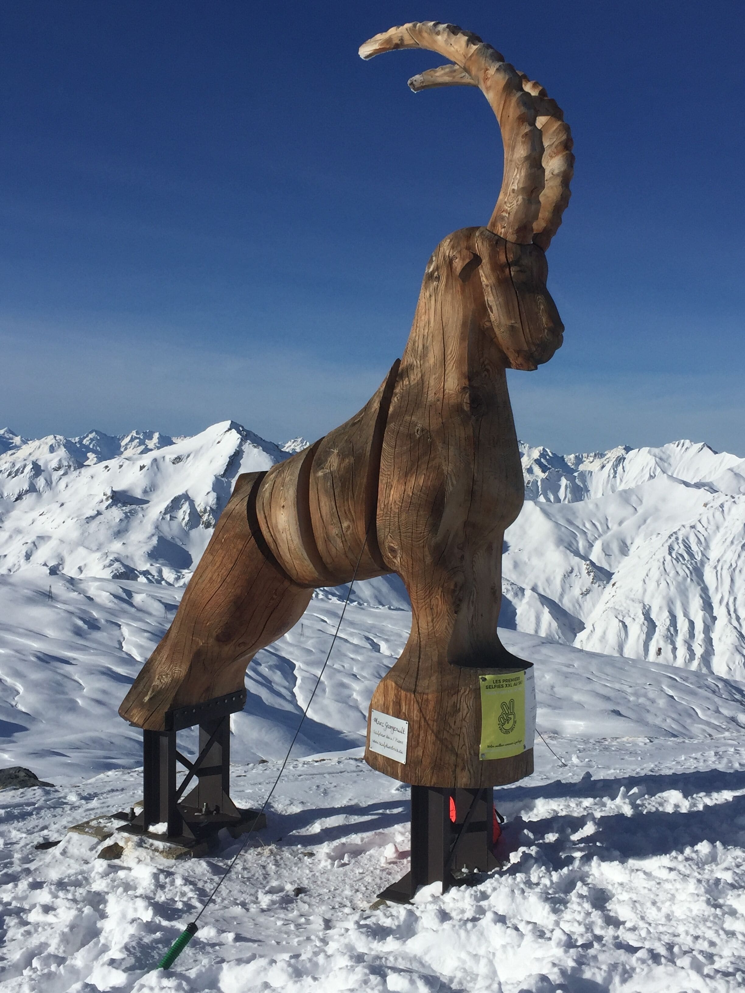 A wooden sculpture of a reindeer on a snowy mountain with a clear sky.
