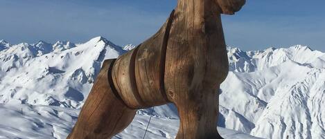 A wooden sculpture of a reindeer on a snowy mountain with a clear sky.