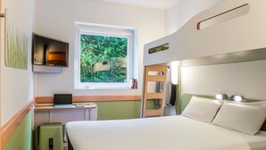 A hotel room with a bed, a desk with a laptop, a window with a view of greenery, and a small stool. - Ibis Budget Bilbao Barakaldo (Barakaldo)