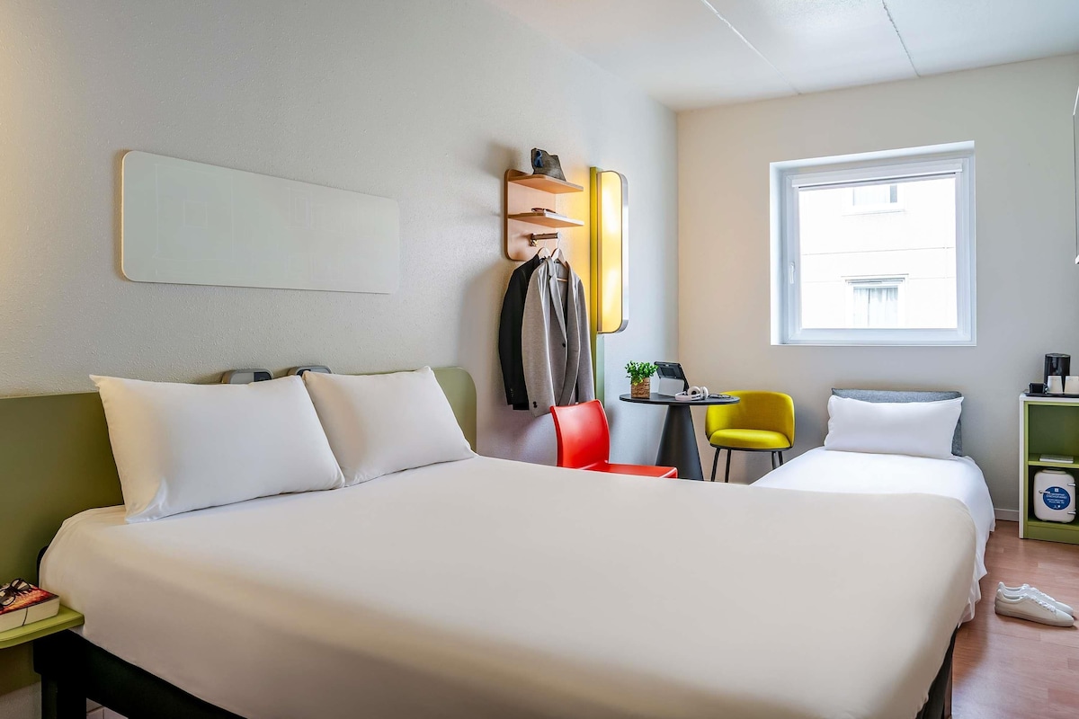 A hotel room with a large bed, a desk with a laptop, a chair, and a window.