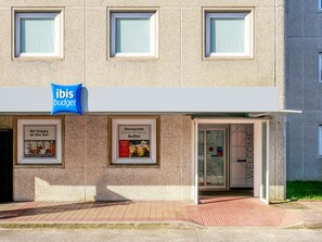 Un edificio con un letrero que dice 'ibis budget' y dos carteles enmarcados que publicitan opciones de desayuno y comidas tipo bufé.