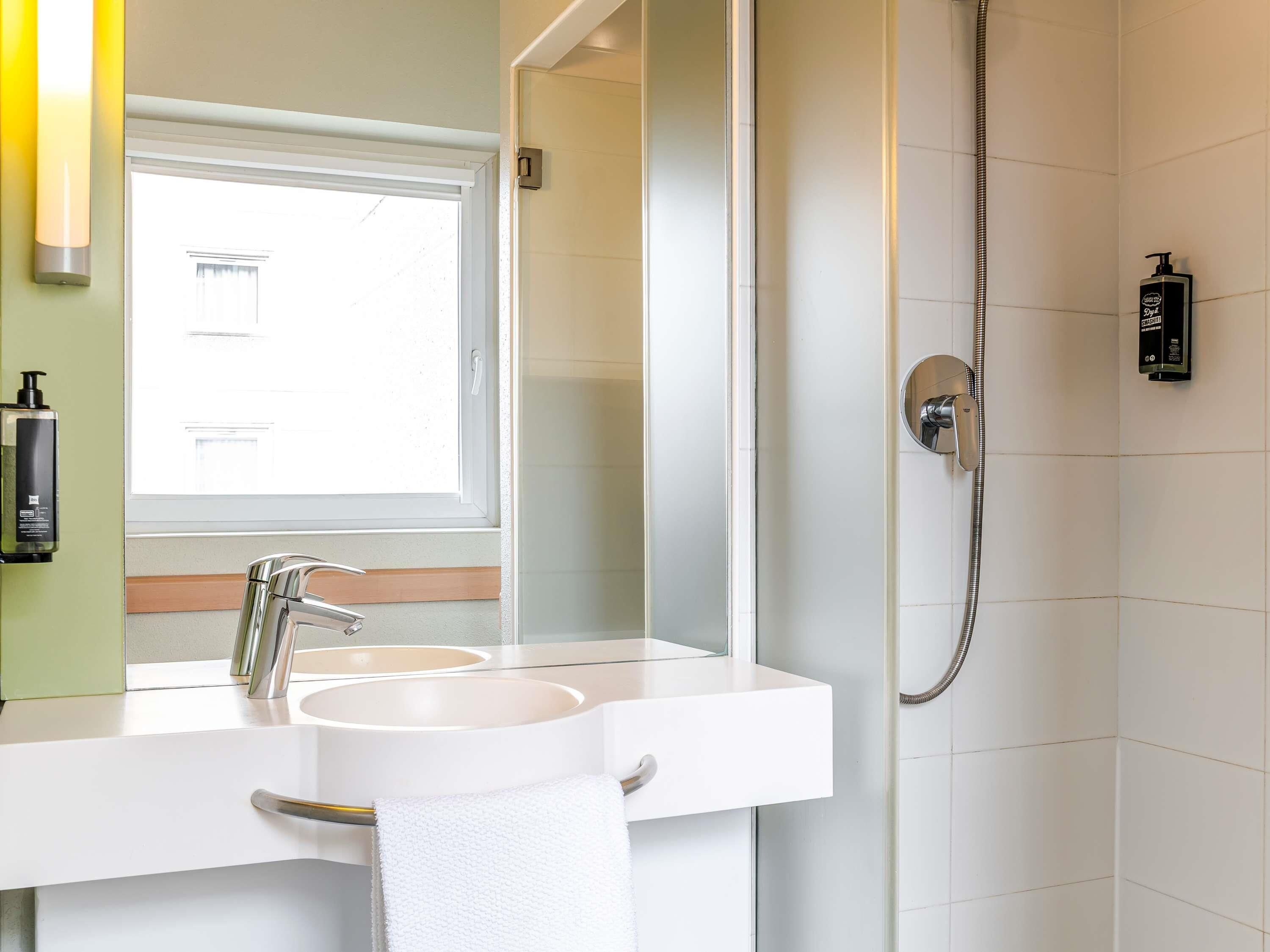 A bathroom with a double sink, a mirror, a shower, and a window.