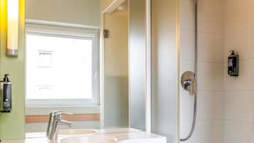 A bathroom with a double sink, a mirror, a shower, and a window.