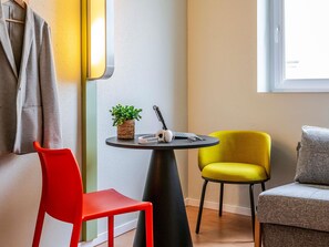 Una habitación con una mesa redonda, una silla roja, una silla amarilla, un sofá gris, un sillón gris y una planta en maceta.