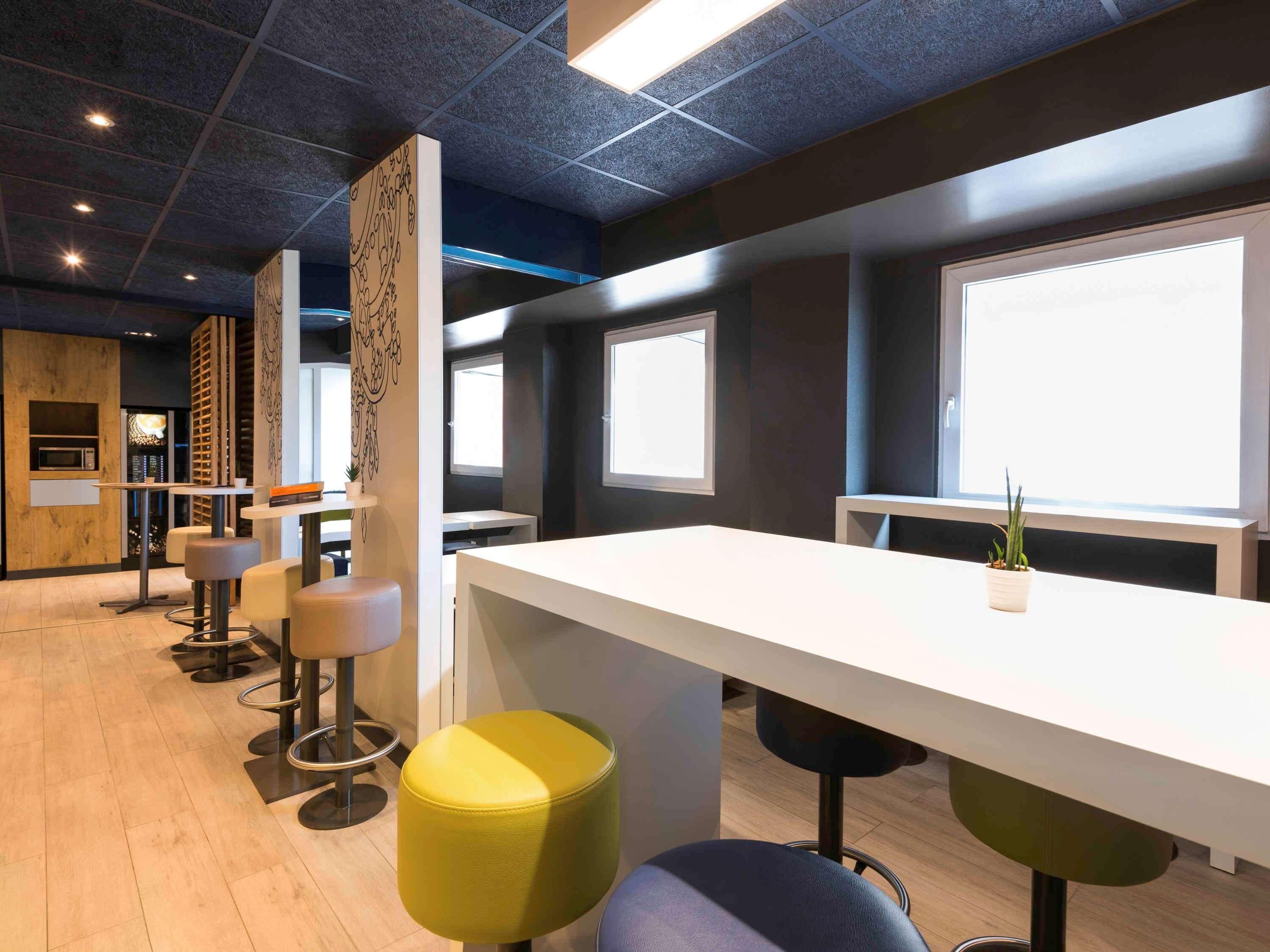 A modern office space with a long white table, multiple stools, and large windows.