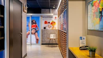 Un pasillo de hotel con un mostrador de recepción de madera, un letrero de KEYS BUX, un mapa en la pared y un cartel que anuncia un bufé de desayuno.