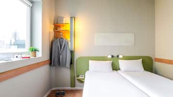 Habitació d'hotel amb un llit, una taula de nit, una làmpada, una finestra amb vistes i un penjador amb una jaqueta.