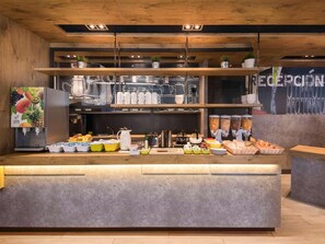 A breakfast bar with a fruit juice dispenser, coffee machine, and various food items.