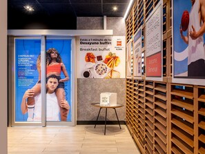 A hotel lobby with a breakfast buffet sign, a key box, and a wooden wall with shelves. - Ibis Budget Bilbao Barakaldo (Barakaldo)