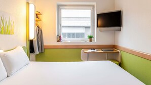 A hotel room with a bed, a desk, a TV, a window with a view, and a plant on the windowsill. - Ibis Budget Bilbao Barakaldo (Barakaldo)