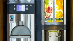 Two coffee machines with digital displays and fruit-themed labels. - Ibis Budget Bilbao Barakaldo (Barakaldo)