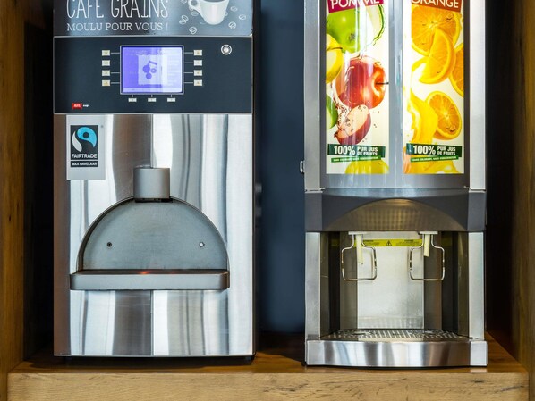 Two coffee machines with digital displays and fruit-themed labels. - Ibis Budget Bilbao Barakaldo (Barakaldo)