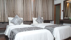 A hotel room with two beds, each with a patterned bedspread and pillows, a wooden floor, and a large mirror on the wall.